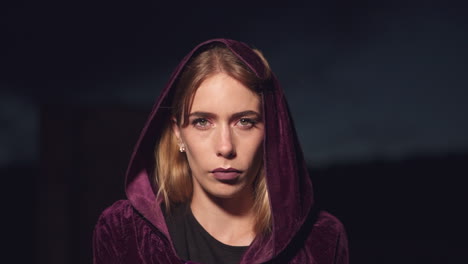 Mysterious-young-blonde-woman-wearing-a-hood-and-a-cloak-and-staring-at-the-camera-with-serious-expression