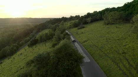 Drone-footage-panning-up-flying-along-road-with-cars-driving-on-Box-Hill,-with-trees-and-greenery-panning-up-to-classic-English-countryside