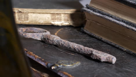Close-up-revealing-pan-of-old-rusty-key-by-books-on-wooden-table