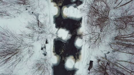 Top-down-aerial-view-of-frosty-forest-river-stream-with-snowy-forest