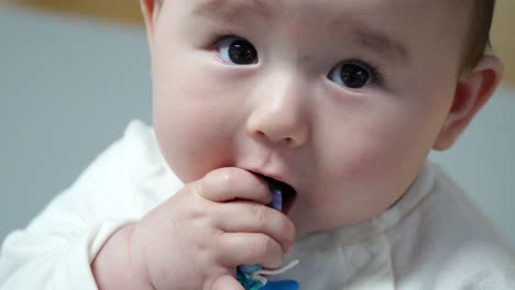 Lindo-Bebé-Tratando-De-Comer-Una-Pulsera-Colorida-Y-Sonriendo-A-La-Cámara,-De-Cerca