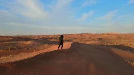 Drone-View:-A-man-walks-alone-in-the-Arabian-Desert-of-the-United-Arab-Emirates,-landscape-video-of-the-gulf-desert,-UAE-desert