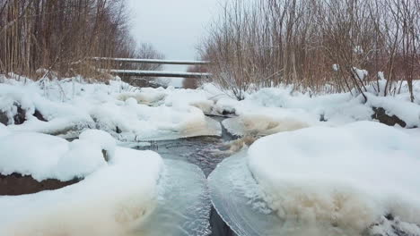 Wild-forest-river-rapids-down-through-frozen-forest-in-drone-tilt-up-shot