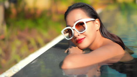 Nahaufnahme-Einer-Glücklichen,-Sinnlichen-Asiatin-Mit-Sonnenbrille,-Die-Die-Sonne-Im-Swimmingpool-Genießt,-Zeitlupe