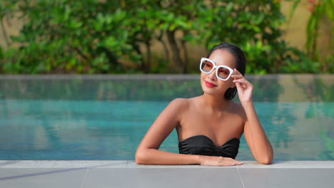 Eine-Schöne-Frau,-Die-Sich-In-Einem-Resort-Schwimmbad-Entspannt,-Passt-Ihre-Sonnenbrille-An,-Um-Eine-Bessere-Sicht-Auf-Ihre-Umgebung-Zu-Erhalten