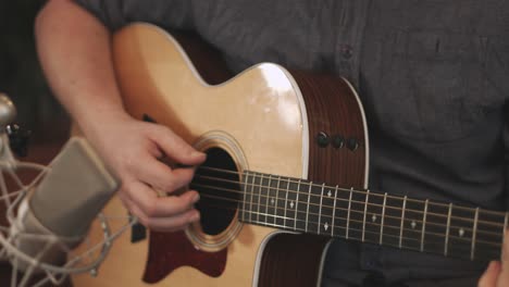 Close-up-of-a-western-acoustic-guitars-body-being-played-by-a-professional-musician-during-a-recording-session-with-a-large-diaphragm-condenser-microphone-placed-in-front