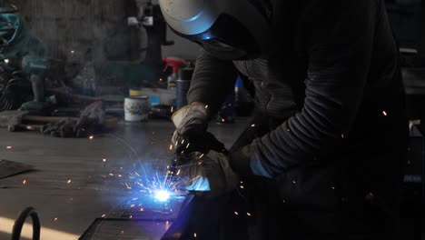 Welder-on-the-table-welds-a-set-of-metal-parts