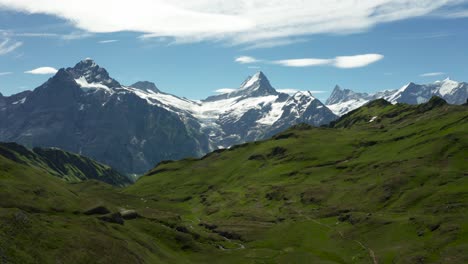 Luftaufnahme-Der-Wunderschönen-Berglandschaft-Mit-Schneebedeckten-Hohen-Berggipfeln-Und-Grünem-Gras-Im-Sommer