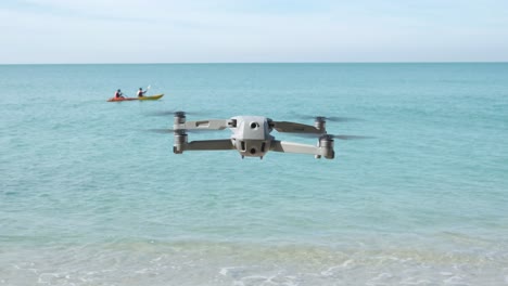 Toma-Estática-De-Un-Dron-Flotando-En-Una-Playa-Con-Océano-Y-Kayakistas-En-Segundo-Plano