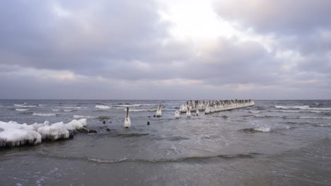 Old-Wooden-Pier-In-Baltic-Sea-Covered-In-Ice-During-Winter-In-A-Cloudy-Day