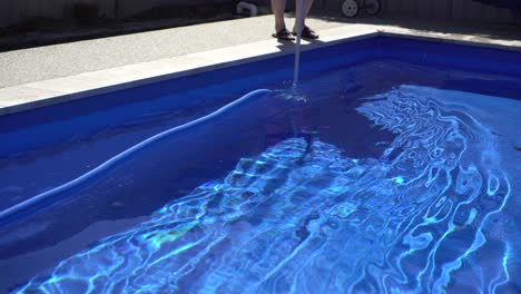 Man-Vacuum-Cleaning-Blue-Pool-In-Backyard