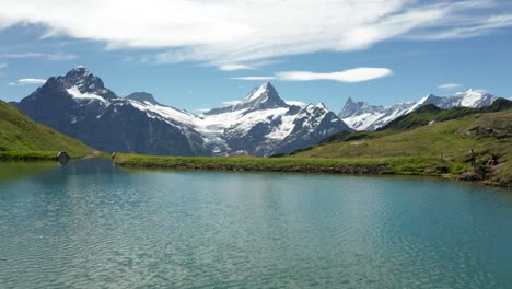 dramatic-close-over-water-aerial-view-of-blue-mountain-lake-in-the-swiss-alps-with-dramatic-snow-covered-mountain-peaks-backdrop,-Bachalpsee-Grindelwald-First,-Switzerland