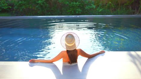 Classy-Female-With-a-Hat-Standing-in-Infinity-Swimming-Pool-Enjoying-in-Tropical-Landscape,-Summer-Fashion-Concept,-Static-Full-Frame