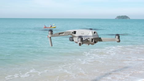 drone-hovering-on-a-beach-with-kayak-and-island-in-background