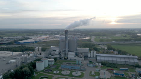Aerial-dolly-of-smoking-factory-chimney-with-a-setting-sun-in-the-background