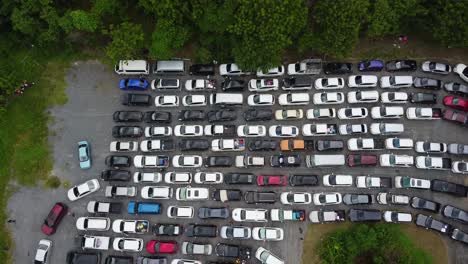 AERIAL:-Drone-Gaining-Altitude-above-a-Parking-Zone-full-by-Cars-surrounded-by-Jungle-forest,-stuck-in-the-Queue-waiting-for-Ferry-from-The-Koh-Chang-Island-to-Mainland,-Thailand,-Asia