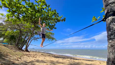 Young-Adult-Male-Slowly-Walking-Along-Slackline-On-Trinity-Beach-In-Cairns