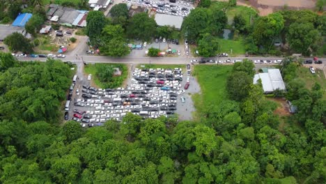 AERIAL:-Revealing-Drone-Shot-of-a-Parking-Zone-full-by-Cars-surrounded-by-Jungle-forest,-stuck-in-the-Queue-waiting-for-the-Ferry-from-Koh-Chang-Island-to-Mainland,-Trat,-Thailand,-Asia