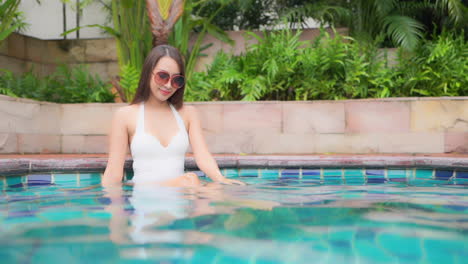 Sophisticated-Trendy-Girl-with-White-Swimwear-Sitting-in-Swimming-Pool