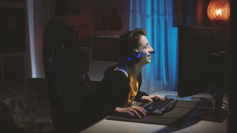 Young-Caucasian-Guy-With-Headset,-Talking-While-Playing-Online-Game-On-The-Computer-Inside-The-Room---medium-shot,-side-view