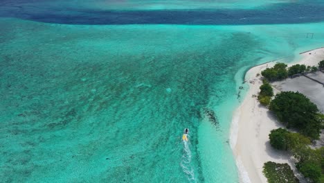 Birdseye-Aerial-View-of-Motorboat-Sailing-By-White-Sand-Beach-of-Maldives-Island-in-Turquoise-Indian-Ocean-Water