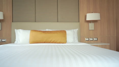 A-slow-pan-across-a-hotel-suite-bed-topped-with-a-gold-covered-decorative-pillow