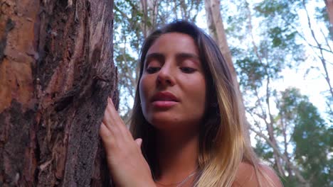 Young-Woman-Touches-Tree-Bark-In-The-Forest---Girl-Looking-Up-While-Touching-The-Rough-Bark-Of-Tree
