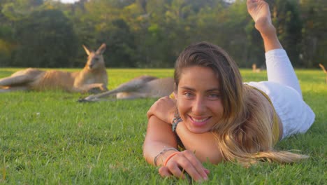 Cheerful-Woman-Lying-On-The-Green-Grass-Together-With-Eastern-Grey-Kangaroos---Gold-Coast,-QLD,-Australia