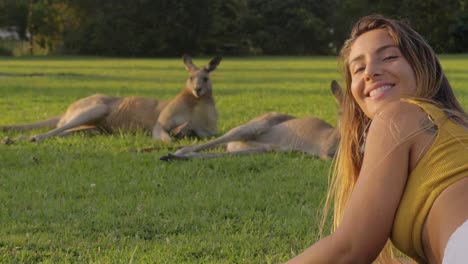 Mädchen,-Das-Auf-Dem-Grünen-Gras-Liegt-Und-Die-östlichen-Grauen-Riesenkängurus-Beobachtet,-Die-An-Einem-Sonnigen-Tag-Ruhen---Mädchen-Dreht-Sich-Um-Und-Lächelt-Süß-In-Die-Kamera---Gold-Coast,-Queensland,-Australien