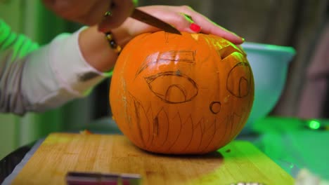 Woman-with-red-nails-carving-eyebrow-into-the-pumpkin-with-colourful-background