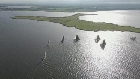 Orbit-drone-shot-of-a-group-of-sailboats-on-the-Sneekermeer-with-the-dutch-countryside-at-the-background