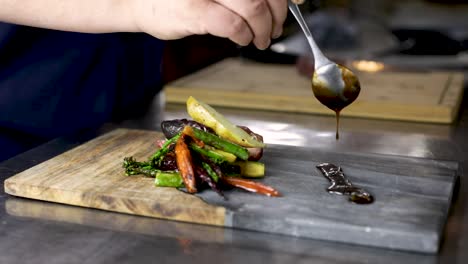 Chef-With-Spoon-Pouring-Tamari-Demi-Glace-Beside-The-Seared-Vegetables