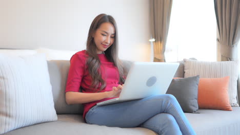 While-sitting-on-a-stylish-comfotable-couch,-a-young-woman-works-on-her-laptop
