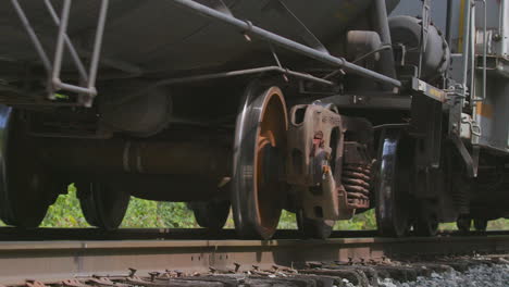 Low-angle-closeup-of-freight-train-car-wheels-and-cars-passing-by-camera