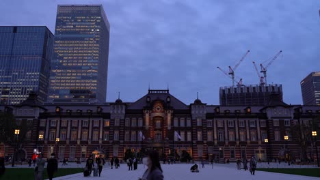 Famous-Tokyo-Station-at-night-with-commuters-moving-around-and-skyscrapers-in-background---wide-frontal-view