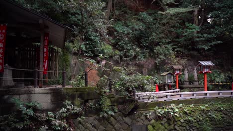 Langsamer-Schwenk-über-Einen-Kleinen-Japanischen-Tempel-Im-Wald-Mit-Typischen-Steinsäulen-Und-Gebäuden