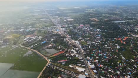 AERIAL:-Establishing-shot:-Drone-Panning-Up-high-above-the-Highway-which-separates-the-Asian-Village,-Nakhon-Ratchasima-Town-in-Korat-Province,-Thailand-Asia