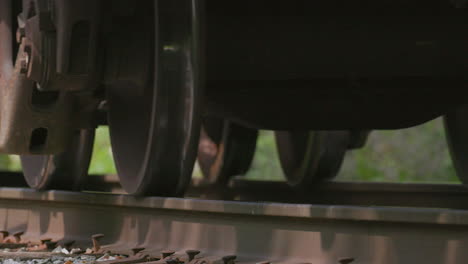 Closeup-on-freight-train-wheels-on-train-tracks-passing-by-camera-from-low-angle-in-slow-motion