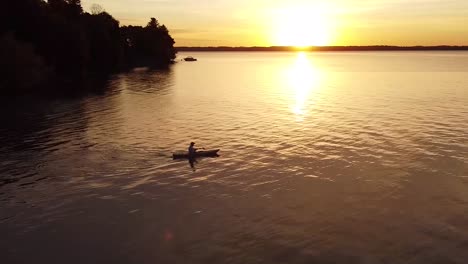 Aerial-shot-of-man-paddling-across-a-lake-at-sunset
