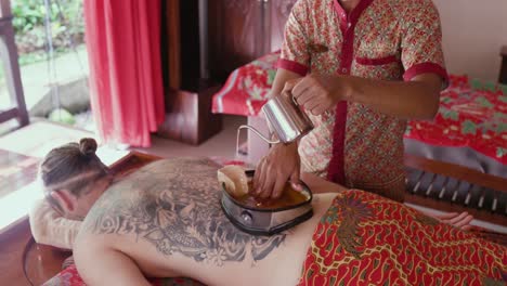 Spa-therapist-pours-oil-into-the-wax-lined-container-on-the-back-on-a-patient-enjoying-a-Kati-Vasti-treatment