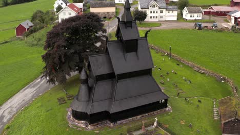 Hopperstad-Stavkyrkje,-Black-Wooden-Stave-Christian-Church-and-Village-in-Norway-Aerial-View,-Ancient-Norwegian-Religious-Monument-From-12th-Century,-Drone-Shot