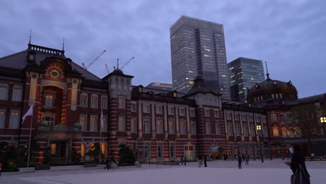 Famous-Tokyo-Station-at-night-with-commuters-moving-around-and-skyscrapers-in-background---wide-side-view