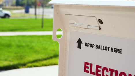 Drop-Ballot-Here-Sign-with-Arrow-and-Slot-for-Mail-in-Election-Voting-Box-with-Person-Walking-and-Car-in-Background