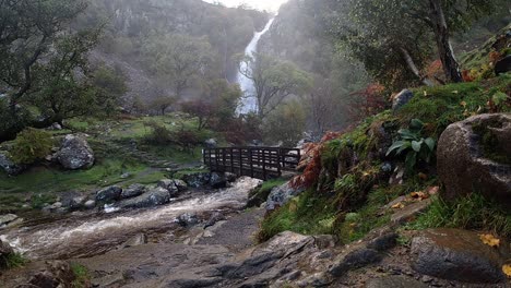 Waterfall-rocky-river-flowing-water-slow-motion-cascading-under-wooden-bridge-in-national-park-wide-view