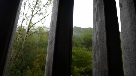 Raining-weather-in-rural-mountain-countryside-through-rustic-oak-wood-barn-beams-window-dolly-right-looking-up