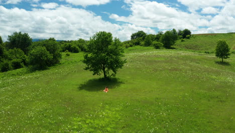 Girl-in-Orange-Dress-relaxing-in-green-fields-of-Lika-Region,-Croatia
