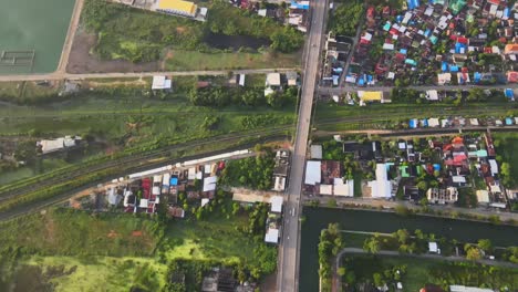 AERIAL:-Drone-Flies-forward-along-the-Highway-which-separates-the-Asian-Village,-Nakhon-Ratchasima-Town-in-Korat-Province,-Thailand-Asia