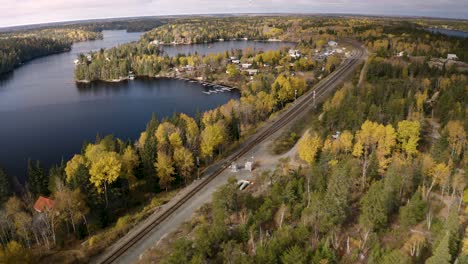 Colorful-aerial-shot-of-train-tracks-and-cottages-along-side-cold-cool-fresh-water-lakes-in-Canada's-beautiful-whiteshell