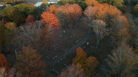 Aerial-shot-of-a-cemetery-surrounded-by-colorful-autumn-trees,-sunset