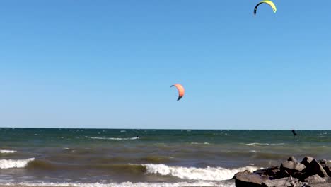 Kiteboarders-on-a-beautiful,-virtually-cloudless-day-traversing-the-shoreline